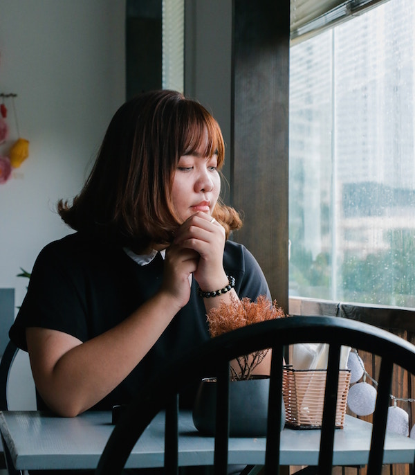 Asian woman sitting at table looking out window